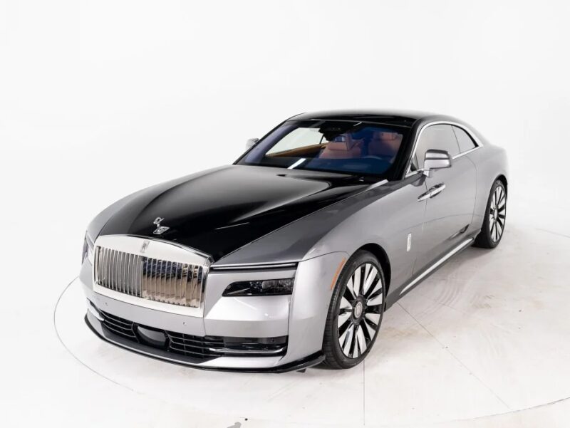 The Rolls-Royce Spectre, a luxury sedan with a glossy black and silver exterior, features a prominent grille and sleek design. This Electric Ultra-Luxe vehicle stands proudly as the ultimate Super Coupe, perfectly displayed against a pristine white background.