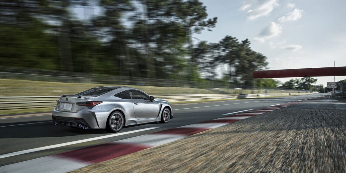 A sleek silver Lexus 2025 RC F Final Edition speeds down a racetrack, surrounded by trees and under a partly cloudy sky.