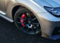 Close-up of a silver Lexus 2025 RC F's front wheel with black alloy rim and red brake caliper, showcasing the sleek design of its Final Edition, parked on asphalt.