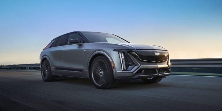 A gleaming 2026 Cadillac Lyriq-V glides along the road at sunset, its sleek design catching the last rays of daylight against a clear sky backdrop.
