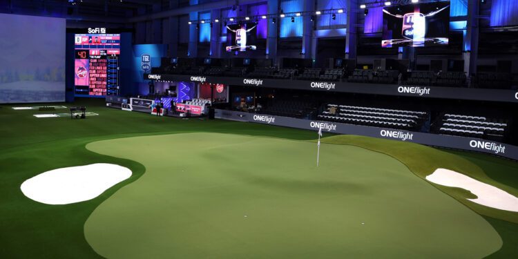 Experience a first-class indoor golf setup featuring a large screen, artificial green, sand traps, and a digital scoreboard all under captivating blue and purple lighting. Perfect your swing and feel like you're part of the TGL elite with this cutting-edge environment.