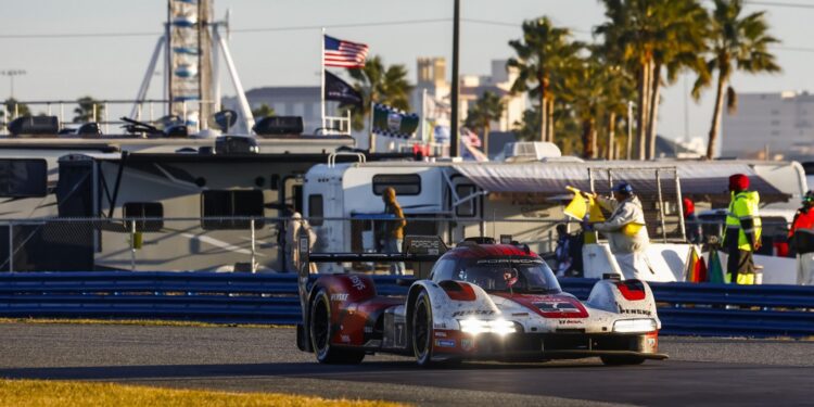 A Porsche race car speeds on the track during the 24 Hours of Daytona, with RVs, spectators, and palm trees in the background on a sunny day.