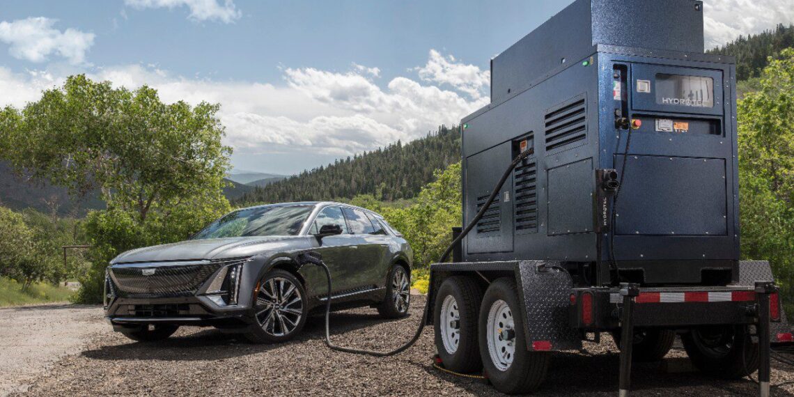 Electric car charging from a portable generator on a dirt road with trees and hills in the background.