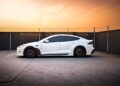 A white Tesla sports car is parked in an open, fenced area under a cloudy orange sky, reminiscent of a scene Joe Rogan might discuss in one of his thought-provoking podcasts.