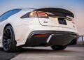 Low-angle view of a white S-APEX sports car with a carbon fiber rear spoiler and custom wheels, parked on a road.