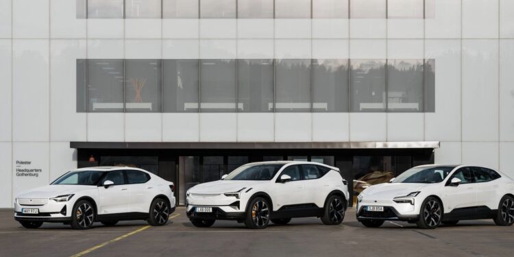 Three white electric cars are parked in front of a modern building with large glass windows.