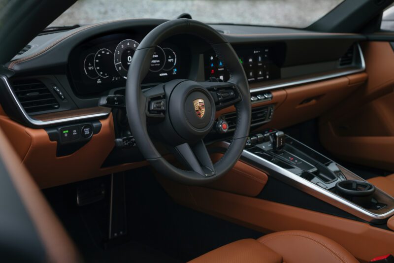 Interior view of a car showing a leather-wrapped steering wheel, digital dashboard, and modern center console with touchscreen controls.