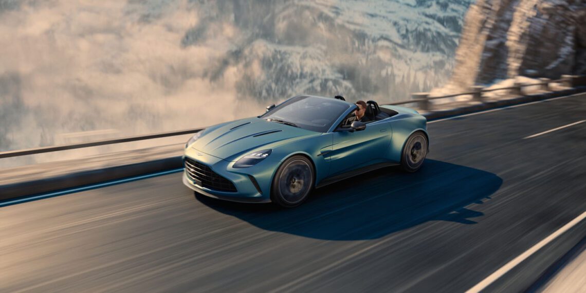 A sleek, blue Aston Martin Vantage Roadster gracefully drives on a mountainous road with snow-covered peaks in the background, capturing the thrill of adventure and the elegance of a new car release.