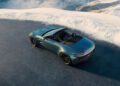 An Aston Martin Vantage Roadster is elegantly parked on a mountain road, framed by a breathtaking snowy landscape in the background.