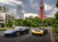 Two groundbreaking sports cars, including the sleek 2024 model from Automobili Pininfarina, are parked on a city street with tall buildings and a red tower in the background.