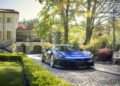 A groundbreaking blue sports car by Automobili Pininfarina, set for 2024, sits elegantly on a cobblestone driveway in front of a villa, surrounded by lush greenery and trees.