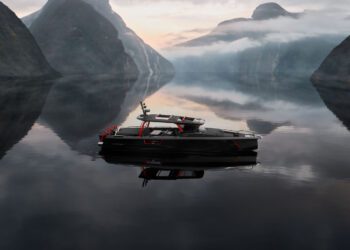 A sleek black boat with red accents, the BRABUS Shadow 1200 Black Ops Signature Edition floats on calm water, surrounded by misty mountains.