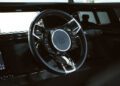 Close-up of a luxury car's steering wheel adorned with the BRABUS "B" emblem, featuring a sleek leather finish and mounted control buttons. Touchscreens glow in the background, embodying the Black Ops Signature Edition style.