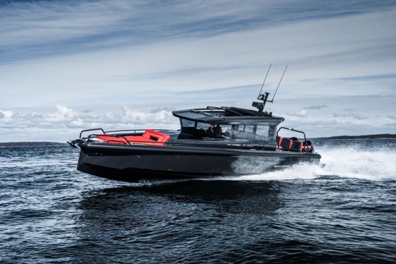 A sleek, black speedboat with red seating moves quickly across a body of water under a cloudy sky, offering an exhilarating maritime experience.