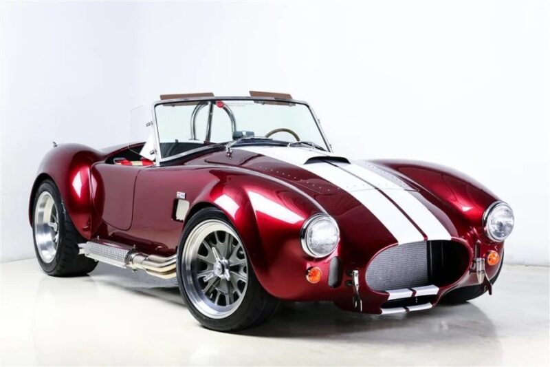 A unique creation, this classic red roadster boasts white racing stripes, chrome wheels, and side exhausts. Displayed in a studio setting, it's an irresistible find for custom car enthusiasts.