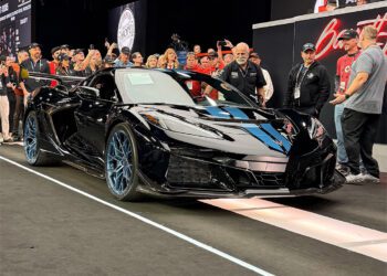 A sleek black Chevrolet Corvette ZR1 is displayed on a stage at Barrett-Jackson in Scottsdale, surrounded by people taking photos and admiring it.