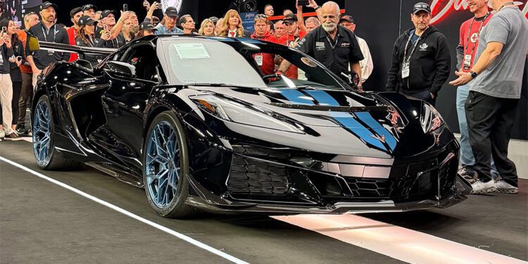 A sleek black Chevrolet Corvette ZR1 is displayed on a stage at Barrett-Jackson in Scottsdale, surrounded by people taking photos and admiring it.