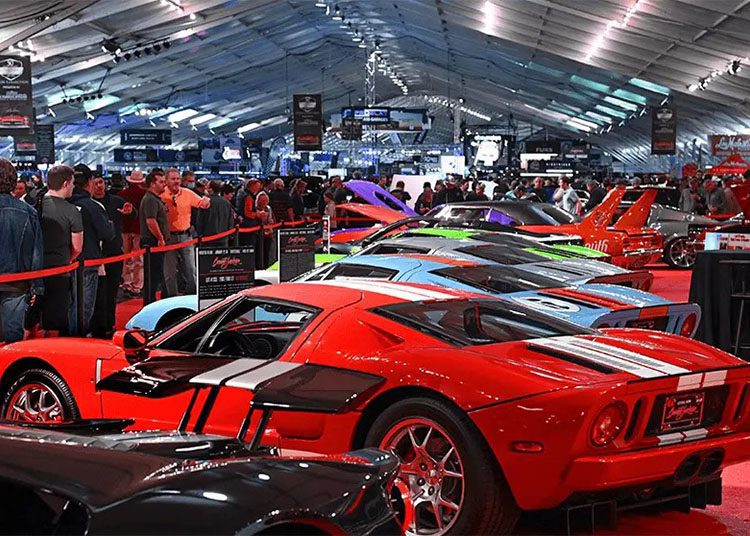 A car show featuring a row of sports cars under a large tent, drawing crowds during Arizona Car Week 2025. Fans gather around, flipping through the latest duPont REGISTRY Guide for details on these stunning vehicles.