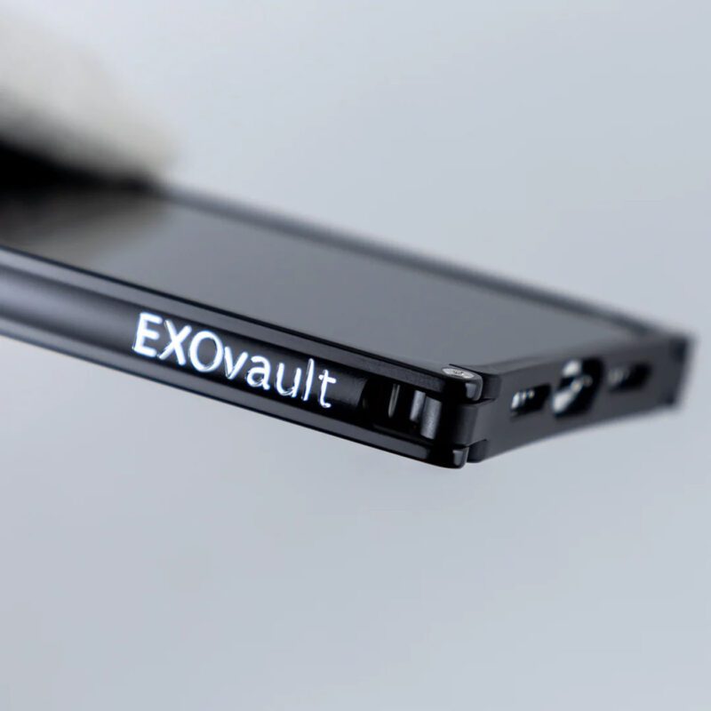 Close-up dari smartphone mewah dengan casing Exovault logam hitam, berlabel elegan dan menampilkan port di samping.