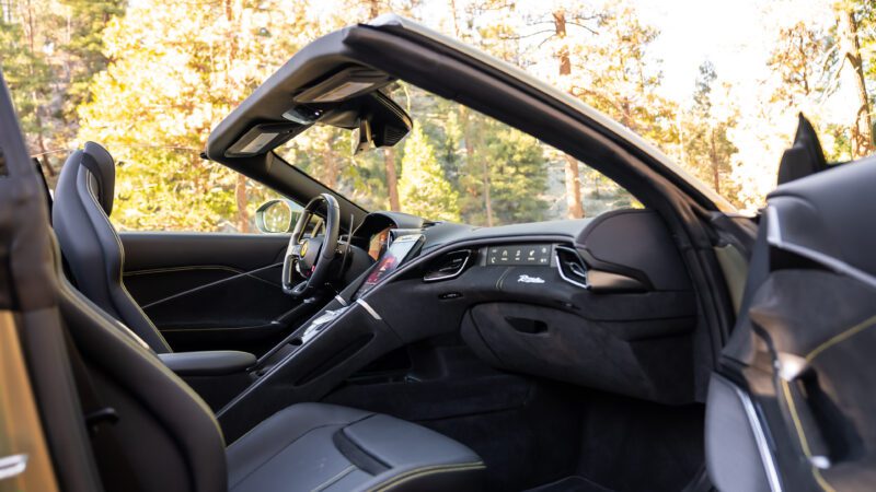 Convertible car interior with black leather seats and a modern dashboard, set against an outdoor background with trees.