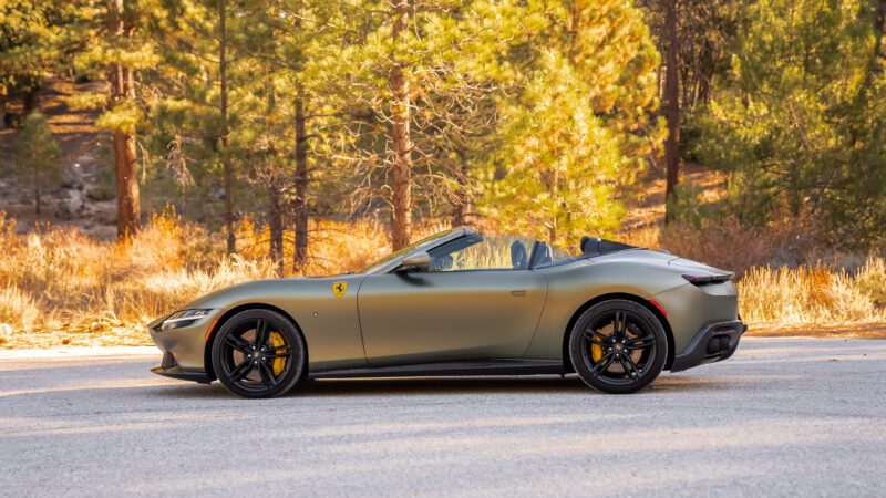 Convertible sports car parked on a road with a forest backdrop.