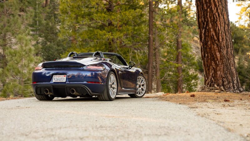 A blue convertible sports car parked on a forest road, surrounded by tall trees.