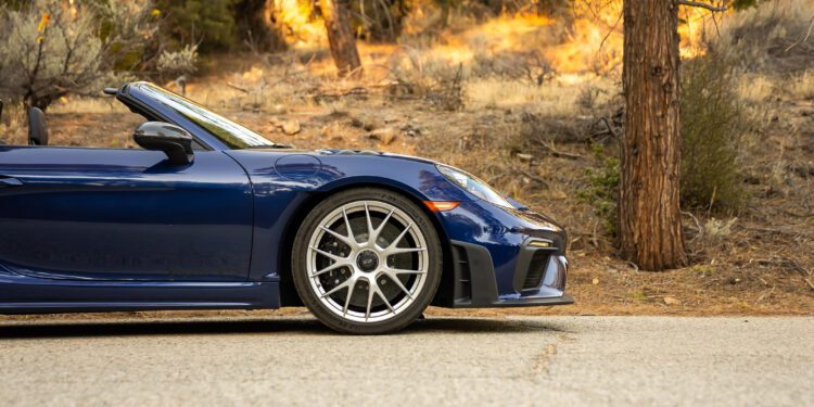 Side view of a parked blue convertible sports car on a road, with a forested background.