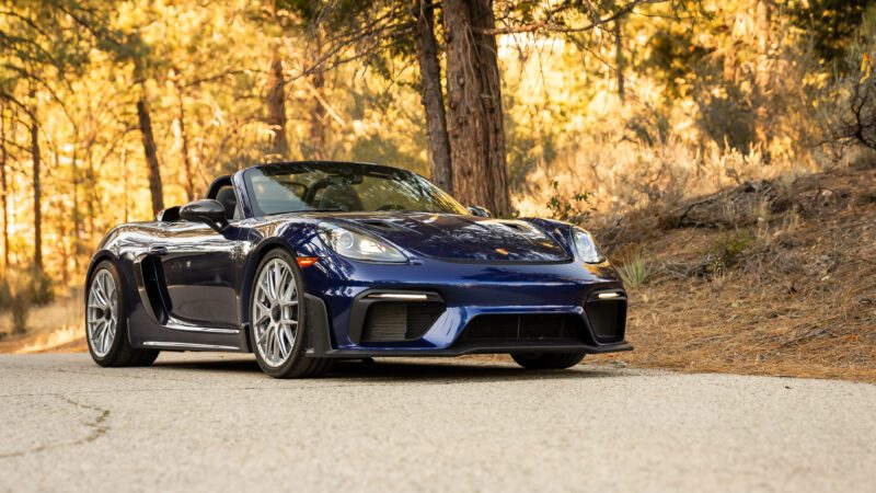 Blue convertible sports car parked on a tree-lined road with sunlight filtering through foliage.