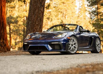 Blue convertible sports car parked on a tree-lined road with sunlight filtering through the trees.