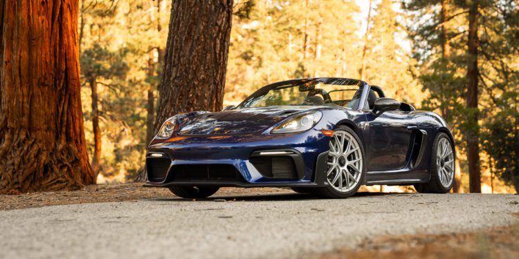 Blue convertible sports car parked on a tree-lined road with sunlight filtering through the trees.