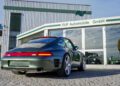 A vibrant green sports car, reminiscent of the iconic 993 Porsche 911, is parked outside RUF Automobile GmbH—a sleek building with large windows and a sign proudly displaying the company's name. LED lighting adds a modern touch to the scene.