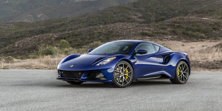 A blue sports car is parked on a road with mountains in the background.