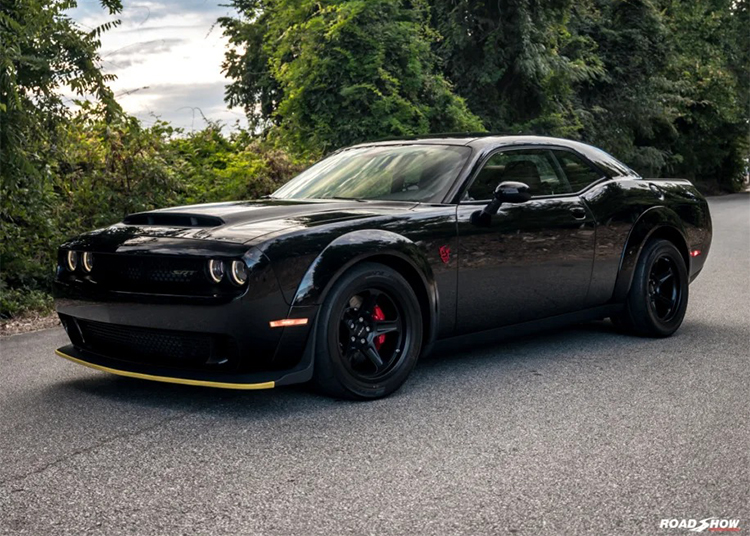 Black sports car parked on a road, surrounded by greenery.