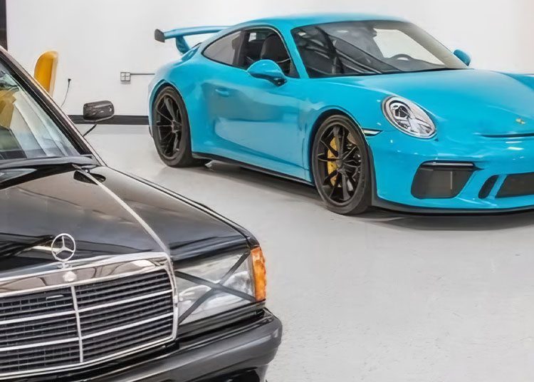 A sleek black Mercedes-Benz is parked alongside a striking blue sports car with a rear spoiler in the garage, reminiscent of the stunning displays at Arizona Car Week 2025 featured in duPont REGISTRY.