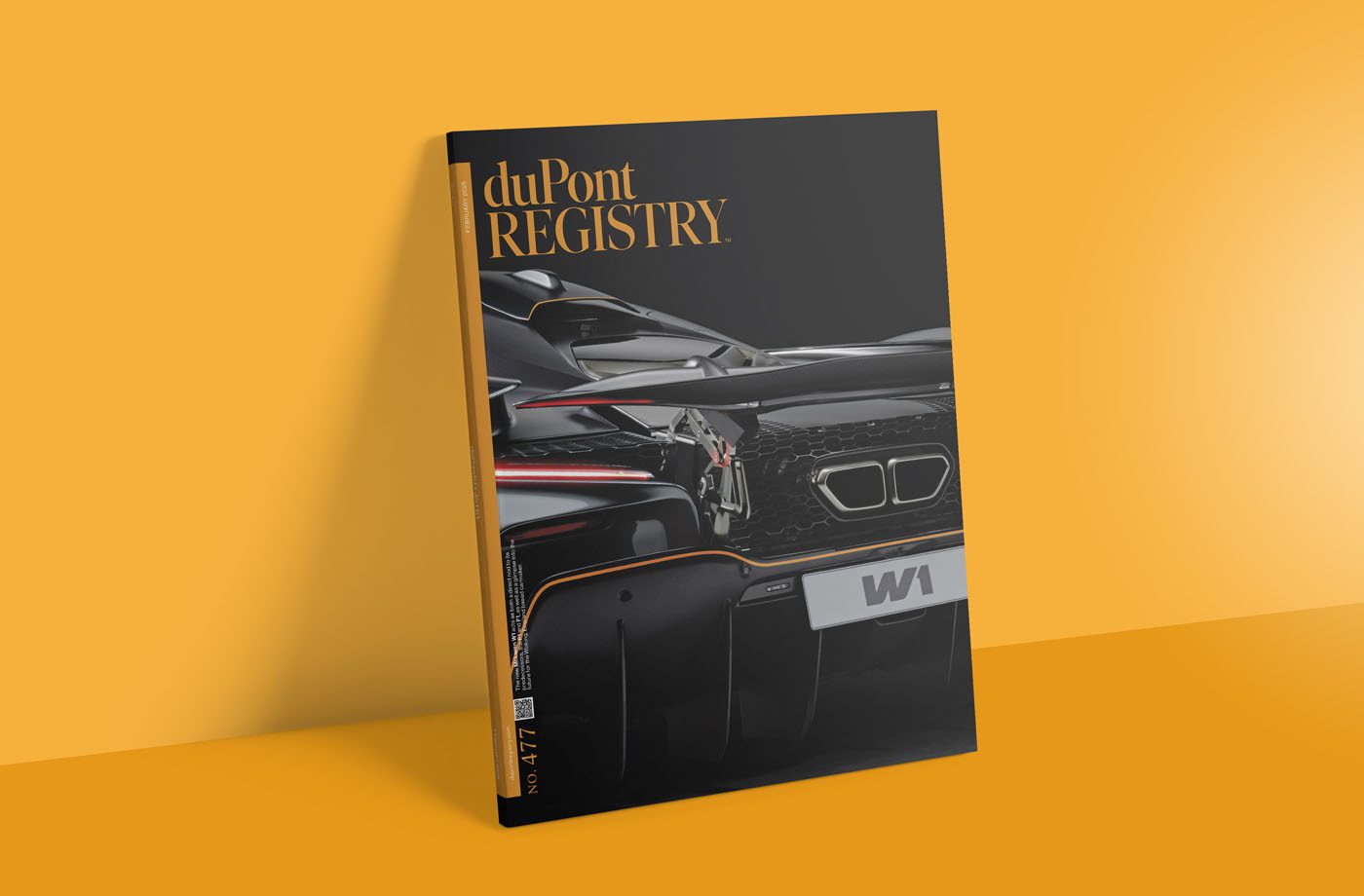 A "duPont REGISTRY" magazine from February 2025 rests on a yellow surface, showcasing the rear end of a sleek black sports car on its cover.