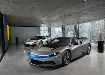 Two groundbreaking 2024 Automobili Pininfarina sports cars sit in a modern showroom with large glass windows, showcasing snowy trees outside. The cars flaunt a sleek silver and black color scheme highlighted by elegant blue accents.