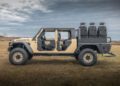 Side view of a modified WARHAWK off-road vehicle with an open cabin and extra seats on the back. Crafted by Hennessey Defense Systems, the rugged machine is parked on grass under a cloudy sky, embodying strength and readiness for any adventure.