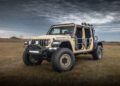 A rugged WARHAWK off-road vehicle with large tires and a beige exterior is parked on an open, grassy field under a cloudy sky, showcasing the might of Hennessey Defense Systems.