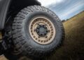 Close-up of a WARHAWK off-road vehicle's tire with rugged tread, positioned on grass under a cloudy sky, showcasing the strength and durability synonymous with Hennessey Defense Systems.