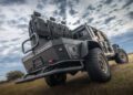 An off-road WARHAWK vehicle with rear-facing seats sits parked on the grass under a cloudy sky, showcasing the robust engineering of Hennessey Defense Systems.