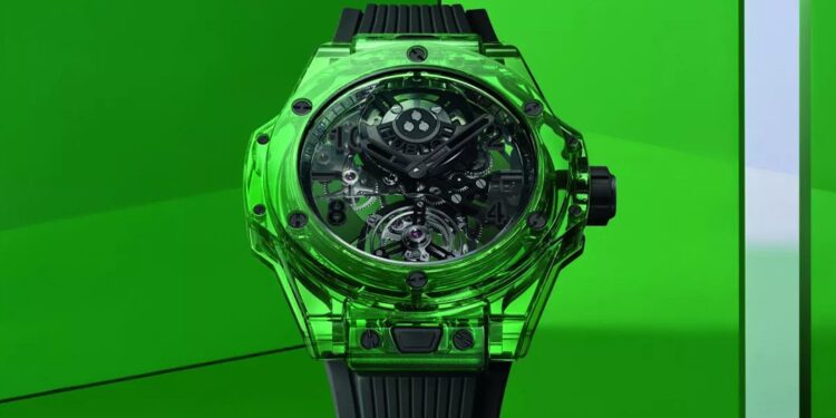 A green transparent watch from Hublot with a visible intricate mechanism and a black band, set against a bright green geometric background, epitomizes the innovation celebrated at LVMH Watch Week.
