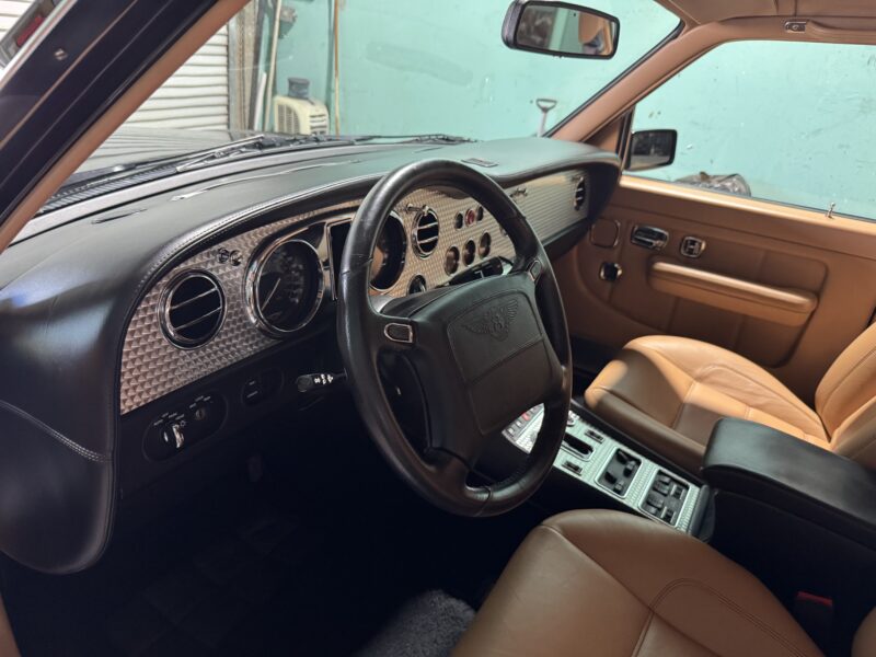 Interior mobil vintage langka ini memancarkan kemewahan dengan dasbor beraksen kayu, kursi kulit mewah, dan roda kemudi yang dihiasi lambang. Mengingatkan pada Bentley Turbo RT, dasbor ini menawarkan berbagai tombol dan kontrol untuk pengalaman berkendara yang indah.