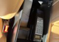 In the plush confines of a Bentley Turbo RT, a luxury armrest storage compartment cradles a vintage car phone with a keypad and display, nestled beside a gleaming seatbelt buckle against rich tan leather seats, echoing the Mulliner craftsmanship.