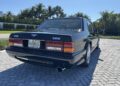 A luxury black Bentley Turbo RT, boasting a Florida license plate, is elegantly parked on a sunlit brick driveway, surrounded by swaying palm trees.