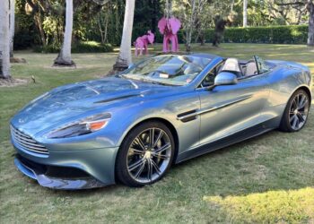 A rare beauty in Ferrari Azzurro Blue, this Aston Martin Vanquish convertible sits elegantly on the grass, with whimsical pink elephant sculptures gracing the background.