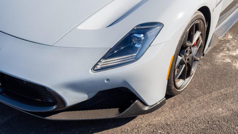 Close-up of a modern gray sports car front, highlighting the headlight, grille, and wheel on a paved surface.