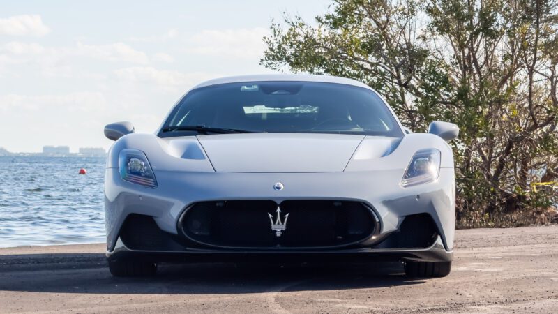 Front view of a silver sports car parked near a body of water with trees in the background.