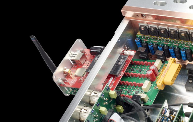 Di dalam perangkat elektronik yang menampilkan berbagai papan sirkuit, modul antena merah, kapasitor, dan konektor, tata letak yang rumit ini menyerupai ketepatan amplifier terintegrasi Dan d'Agostino dari sistem audio utama.