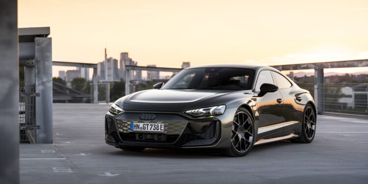 A sleek, black sports car is parked on a rooftop with a cityscape and sunset in the background.