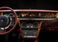 Experience bespoke luxury with a striking red steering wheel, an ornate wood dashboard, and a sophisticated control panel in this Rolls-Royce interior. Every detail exudes elegance, crafting a driving experience like no other.